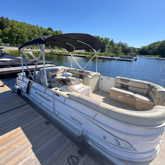 A luxury pontoon boat docked at a wooden dock with a clear blue sky in the background.