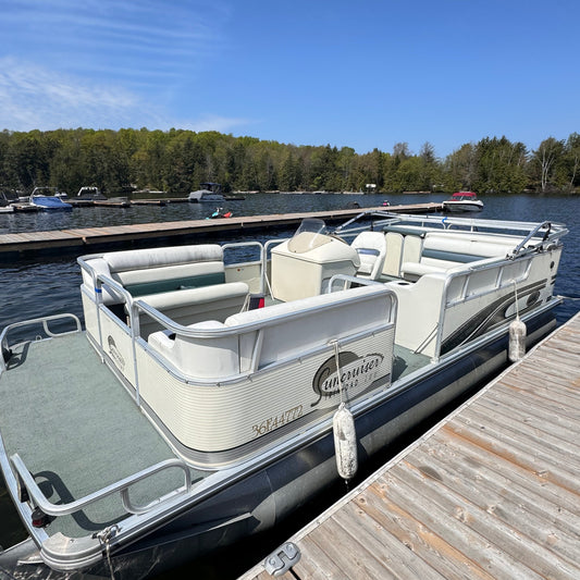 Pontoon boat docked at a wooden dock with clear blue sky and trees in the background
